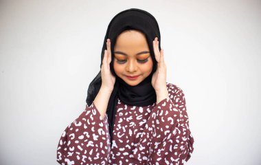 Meyveli, tesettürlü, beyaz arka planda başı ağrıyan genç bir Asyalı kadın.