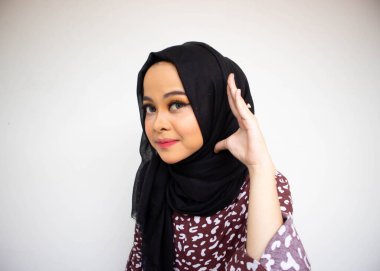 Asyalı müslüman kadın portresi gülümseyen ve işitme hareketi yapan, el kulağına koy, dikkatlice dinle, beyaz üzerine izole edilmiş.