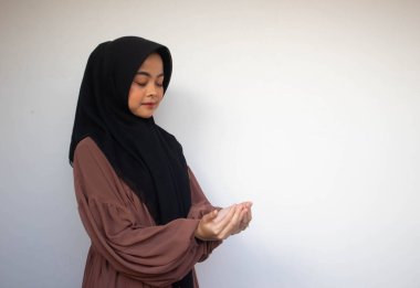 Genç Asyalı Müslüman kadın başörtüsü ve başörtüsü içinde elleri havada gülümseyen yüzüyle dua ediyor. Endonezyalı kadın. Din dua kavramı beyaz arkaplanda izole edildi.