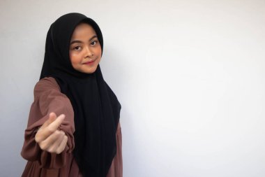 Asyalı güzel tesettürlü kız aşk Kore işaretini parmak ile gösteriyor. Arka planda bulanık, izole beyaz bir zemin var. Endonezyalı Kadınlar