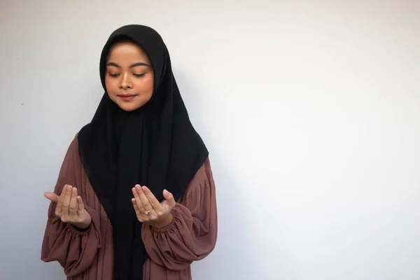 Young Asian Islam Muslim woman in headscarf and hijab prays with her hands up in air with smiling face. Indonesian woman. Religion praying concept isolated on white background.