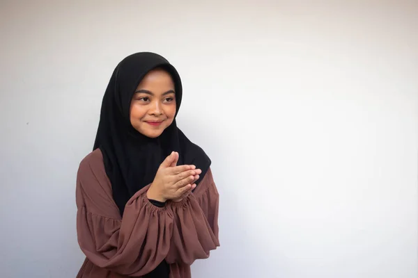 Young Asian Islam woman wearing headscarf gives greeting hands at with a big smile on her face. Indonesian woman on gray background. Eid Mubarak / Eid Fitr / Eid Al-Fitr greeting