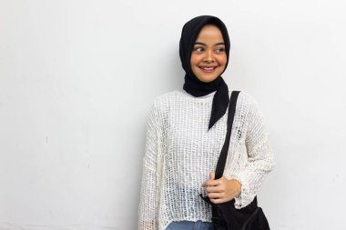 Beautiful smiling hijab woman in casual white shirt carrying the bag looking confident isolated over gray background. College students concept