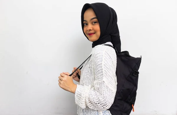 Beautiful smiling hijab woman in casual white shirt carrying the backpack looking confident isolated over gray background. College students concept