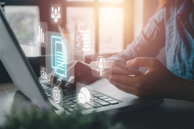 Atılgan Kaynak Planlama ERP, sanal ekrandaki simgelerle belge yönetimi kavramı, ofis masasındaki sanal ekranda dizüstü bilgisayarla çalışan iş kadını.