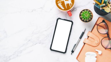 Üst manzara, kulaklıklı beyaz mermer ofis masası, boş ekran akıllı telefon, kalem, defter ve kahve fincanı, kopyalama alanı..