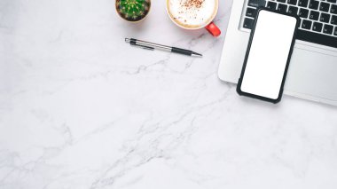 Top view, White marble Office desk with laptop computer, Blank screen smart phone, cup of coffee and pen, copy space, Mock up...	