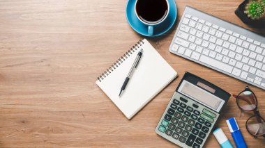 Üst manzara, klavye, not defteri, kalem, gözlük, hesap makinesi ve kahve fincanı, kopyalama alanı olan ofis ahşap masası..