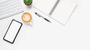 Üst görünüm, klavye bilgisayarlı beyaz ofis masası, boş ekran akıllı telefon, bir fincan kahve, kalem ve defter, kopyalama alanı....