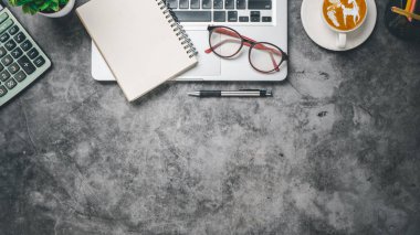 Top view, Dark Office desk with laptop computer, cup of coffee, pen, eyeglass, calculator and notebook, copy space, Mock up...	