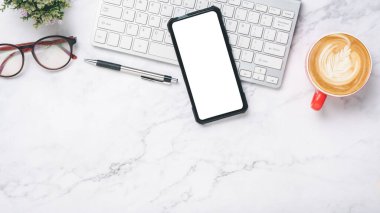 Üst görünüm, klavye bilgisayarlı beyaz ofis masası, boş ekran akıllı telefon, bir fincan kahve, gözlük ve kalem, kopyalama alanı..