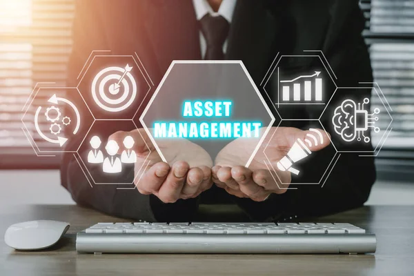 Asset management Business technology internet concept, Businessman hand holding virtual screen asset management icon on office desk workplace.