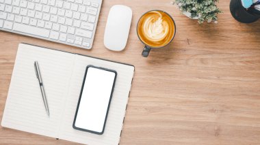 Wooden desk workplace with blank screen smart phone, notebook, keyboard, mouse, pen and cup of coffee, Top view flat lay with copy space.
