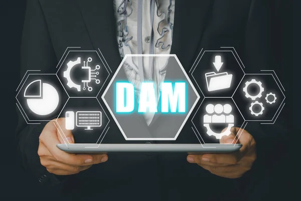 DAM, Digital Asset Management Organization Concept, Person hand using digital tablet with Digital Asset Management icon on virtual screen.