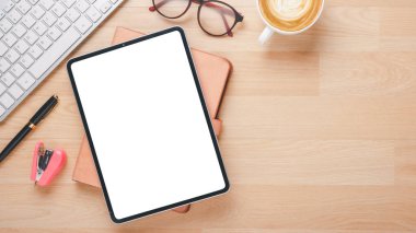 Boş ekran tableti, klavyesi, defteri, gözlüğü, kalemi ve kahvesi olan ahşap masa başı işyeri..