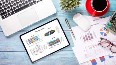 Çizelge ve raporlarla dolu tablet, hesap makinesi, kalem, defter ve kahve çalışma masasında. Üst görünüm düzlüğü kopyalama alanı ile yatıyordu.