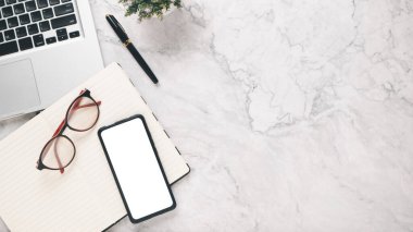 Boş ekran akıllı telefonu, defteri, gözlüğü, bilgisayarı, bilgisayarı ve kalemi olan beyaz ofis masası çalışma yeri..