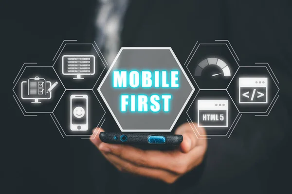 Mobile first concept, Person hand using smart phone with mobile first icon on virtual screen, Digital marketing, office desk.
