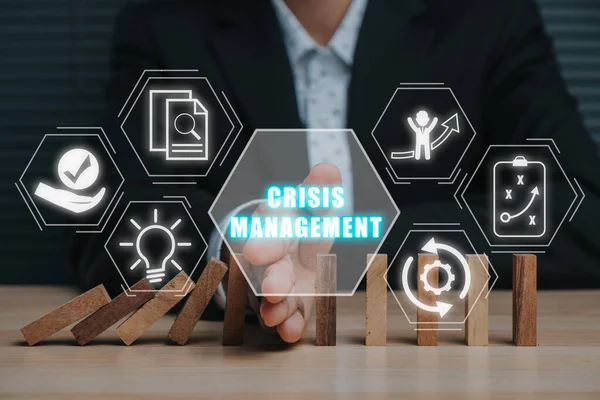 Crisis management concept,  Business person stopping falling dominos with his hand on desk with crisis management icon on virtual screen.