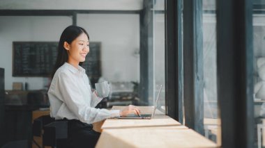 Çalışma alanında dizüstü bilgisayarda çalışan genç bir iş kadını çalışma alanında kahve fincanı tutan bir kadın..