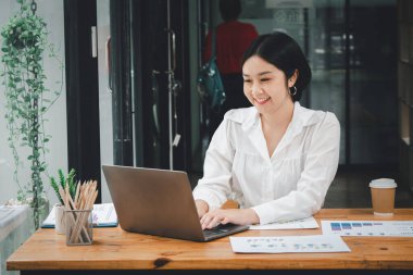 Beyaz gömlekli bir iş kadını dizüstü bilgisayar kullanıyor ve ofisteki masada oturuyor..