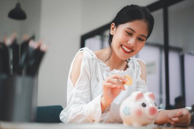 Genç Asyalı kadın, gelecek planları için para biriktirmek amacıyla kumbaraya para sokuyor. finansal yatırım kavramı