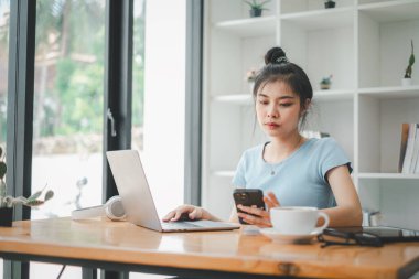 İş kadını telefonda mesaj atıyor ve laptopla çalışıyor. İş yerinde oturan genç ve güzel bir iş kadını. Gülümseyen iş kadını.