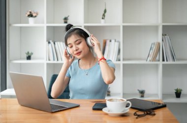 Güzel genç bir kadın dizüstü bilgisayarla müzik dinliyor ve evdeki sandalyede otururken dinleniyor..