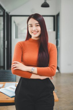 Kollarını kavuşturup kameraya bakan genç bir kadının portresi. Yaratıcı ofiste duran mutlu kız. Fotokopi alanı olan başarılı bir iş kadını.