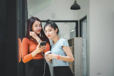 Two young asian women listening to music on couch in living room at home. Happy two asia female using smart phone.	