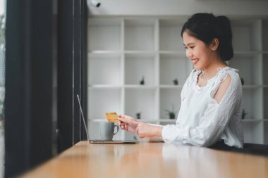 Kredi kartı tutan ve dizüstü bilgisayar kullanan genç bir kadın. Evde çalışan bir iş kadını. Çevrimiçi alışveriş, e-ticaret, internet bankacılığı, harcama.