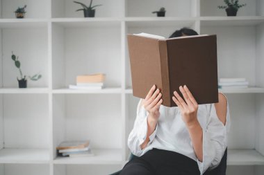 Kapalı kapılar ardında rahat koltukta oturan Asyalı kadın. Güzel genç bayan heyecanlı hikayeler okuyor, tembel sabahların tadını çıkarıyor.,