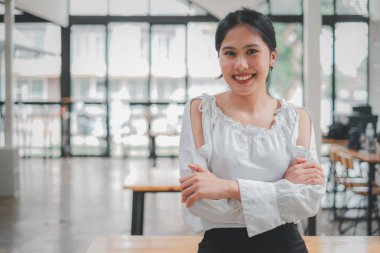 Successful businesswoman standing in creative office and looking at camera. Woman entrepreneur in a coworking space smiling.	