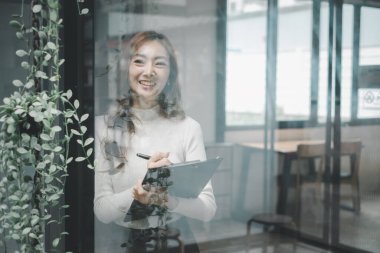 Pencereden dışarı bakan mutlu Asyalı genç satış elemanı. Gülümseyen kadın yönetici, sekreter profesyonel iş hizmetleri sunuyor ofisinde bir fincan kahve tutuyor. Portre