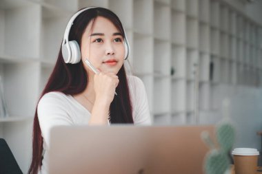 Güzel genç bir kadın dizüstü bilgisayarla müzik dinliyor ve evdeki sandalyede otururken dinleniyor..