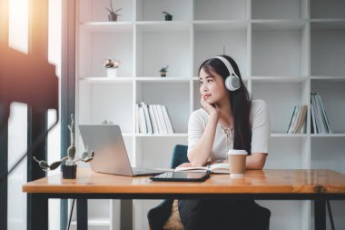 Güzel genç bir kadın dizüstü bilgisayarla müzik dinliyor ve evdeki sandalyede otururken dinleniyor..