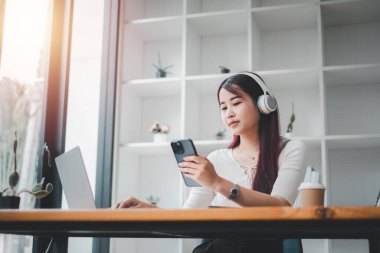 Güzel, genç bir kadın akıllı telefonuyla müzik dinliyor ve evde sandalyesinde otururken dinleniyor..