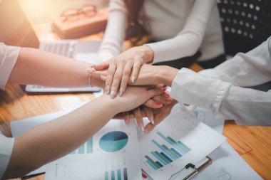 Pozitif çeşitlilikteki iş adamları ellerini birbirinin üstüne koyup birlik ve takım çalışması gösteriyor.