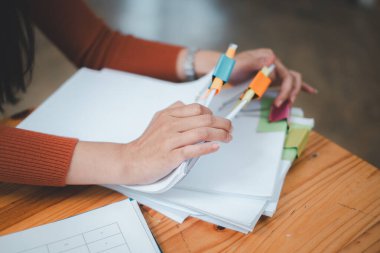 İş kadını elleri, yoğun çalışma masasındaki klasörlerde tamamlanmamış belgelerin aranması ve kontrol edilmesi için kağıt yığınlarında çalışır.