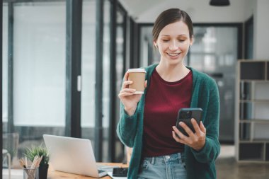 Attractive young woman talking on the smart phone and smiling while standing in office.
