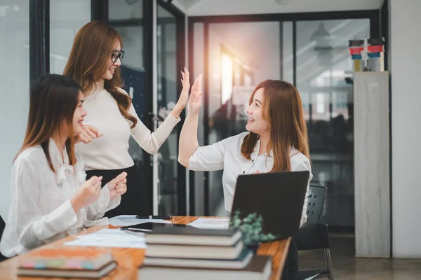 Business team giving a high five to female colleague in meeting. Business professionals high five during a meeting in boardroom.