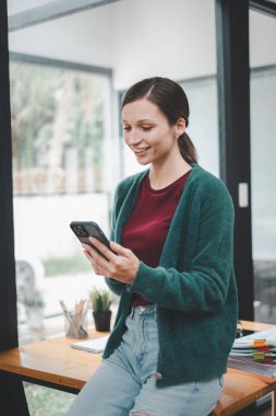 Attractive young woman talking on the smart phone and smiling while standing in office.
