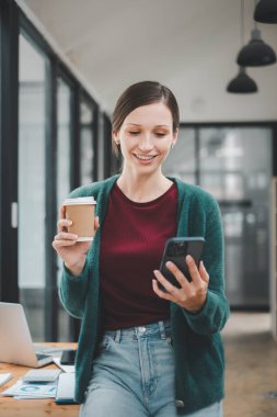 Attractive young woman talking on the smart phone and smiling while standing in office.