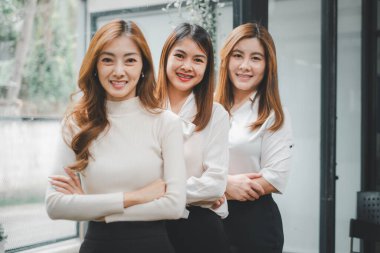 Üç mutlu iş kadını ofis masasında oturuyor ve kameraya, portreye bakıyor.