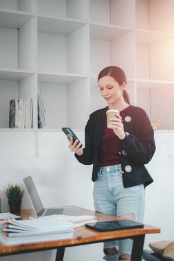 Attractive young woman talking on the smart phone and smiling while standing in office.