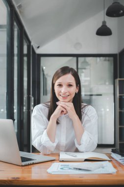Successful businesswoman sitting in creative office and looking at camera. Woman entrepreneur in a coworking space smiling.	