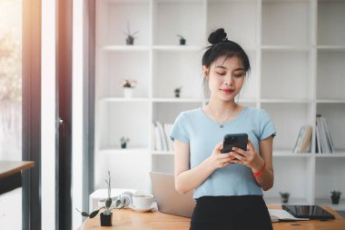 Attractive young woman talking on the smart phone and smiling while standing in office.