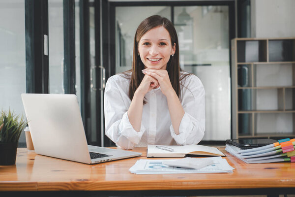 Portrait of young smiling woman looking at camera with crossed arms. Happy girl sitting in creative office. Successful businesswoman standing in office with copy space.