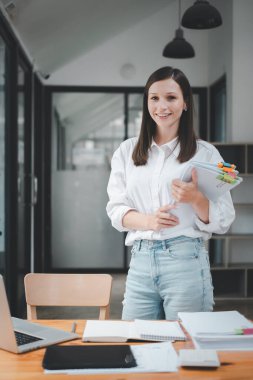 Successful businesswoman standing in creative office and looking on camera. Woman entrepreneur in a coworking space smiling.	