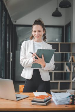 Başarılı iş kadını yaratıcı ofiste dikilip kameraya bakıyor. İş yerinde çalışan kadın girişimci gülümsüyor..